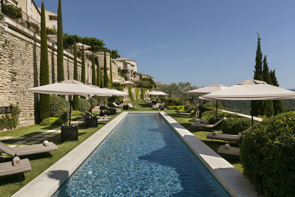 The long swimming pool at Airelles La Bastide surrounded by loungers, umbrella pines and stone walls