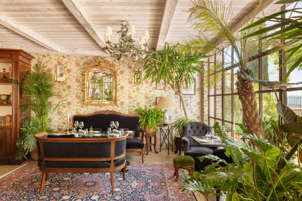 Elegant plant-filled interior dining room at Airelles La Bastide with period furnishings and floral wallpaper