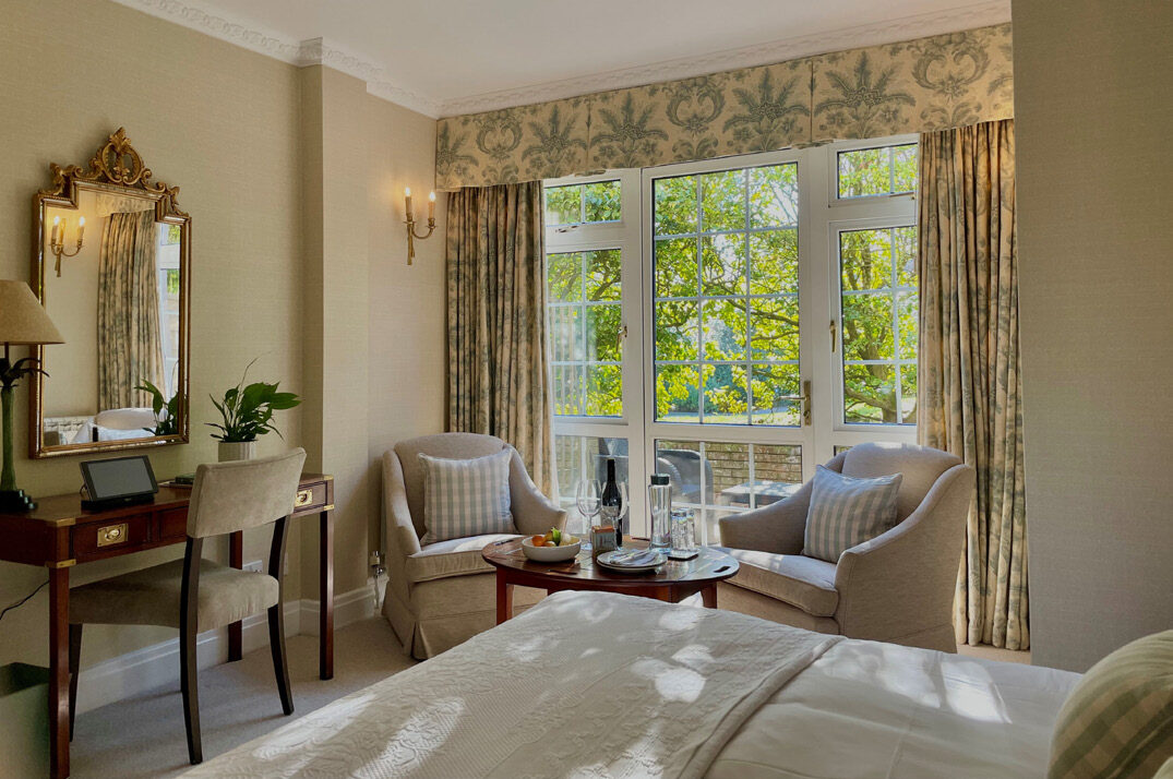 Elegant bedroom at Longueville Manor with garden views, period furniture and floral curtains
