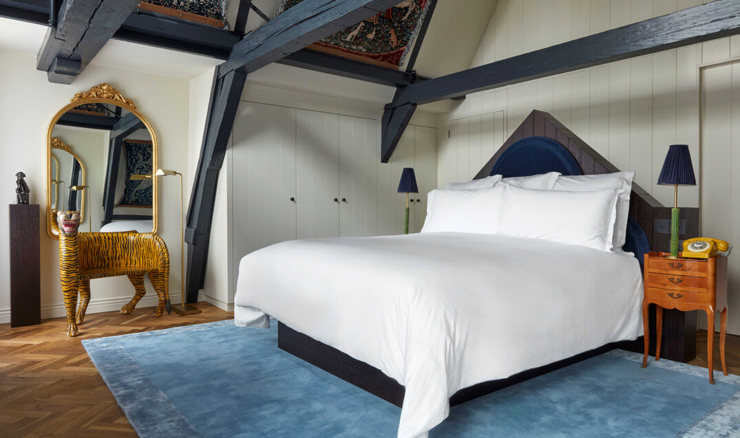 An individually designed guest room at Pulitzer Amsterdam with blue rug, exposed beams and eclectic decor