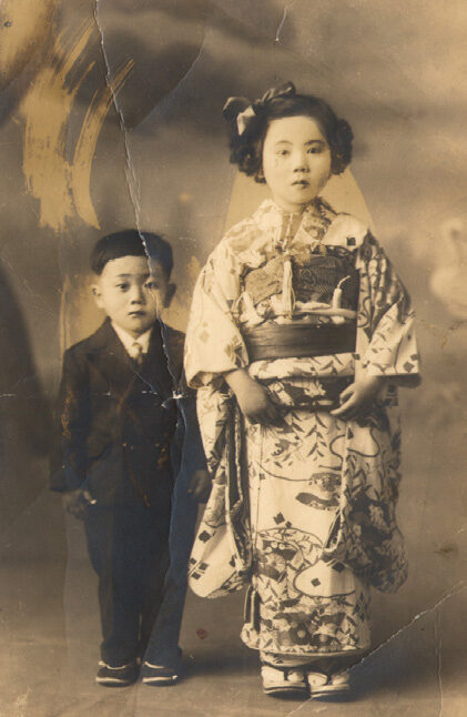 A vintage sepia photograph of two young Japanese children, a boy in a suit and a girl in a kimono