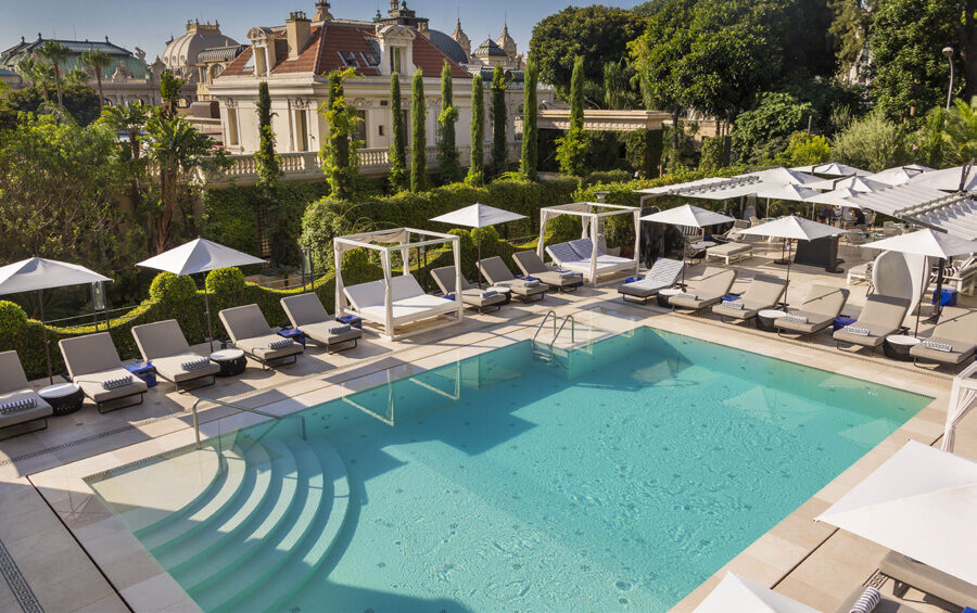 The Odyssey pool at Hôtel Métropole Monte-Carlo, surrounded by sun loungers, white parasols and manicured hedges
