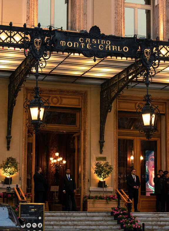 The illuminated entrance of Casino de Monte-Carlo at night, with doormen standing at the ornate entrance