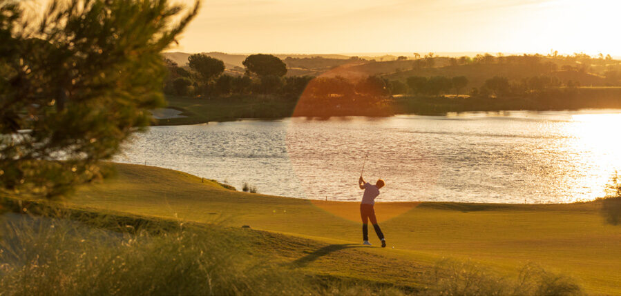 A golfer swinging at sunset on the Monte Rei golf course beside a shimmering lake
