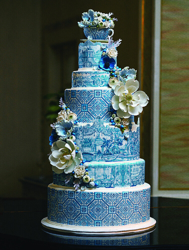 A towering six-tier wedding cake decorated with blue and white azulejo tile patterns and sugar flowers